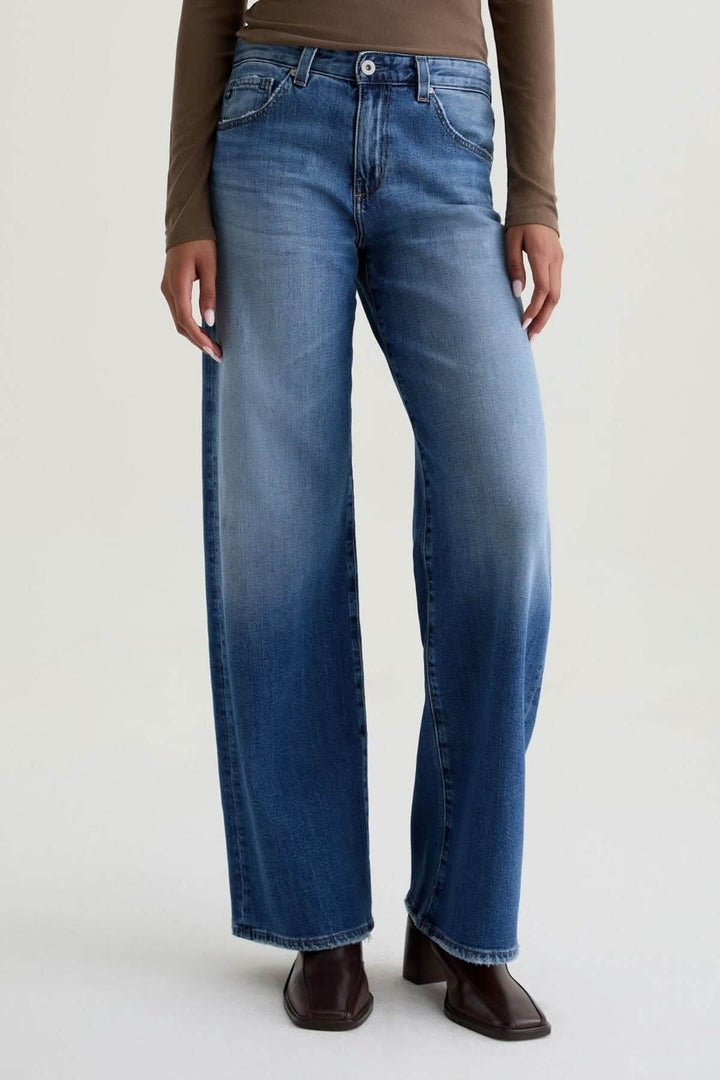 Jean à jambe large bleu avec délavage moyen, coupe ample confortable, porté avec un haut brun et des bottines sombres.