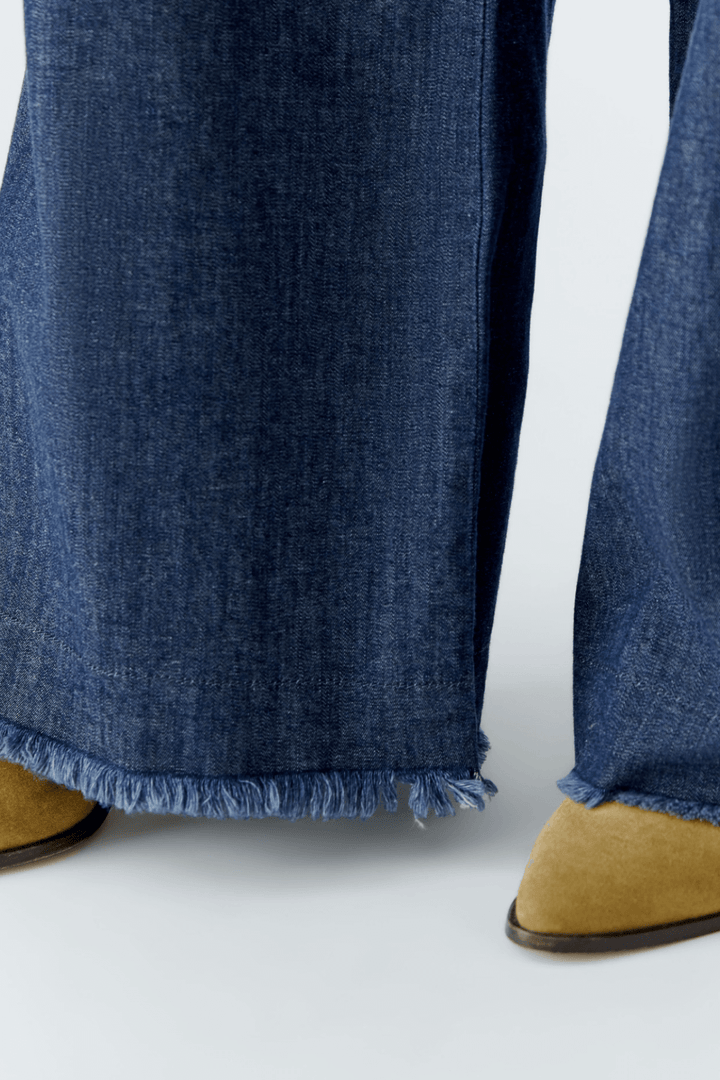 Détail du jean ultra léger avec coupe large et frange en bas, présenté avec des chaussures en daim beige.