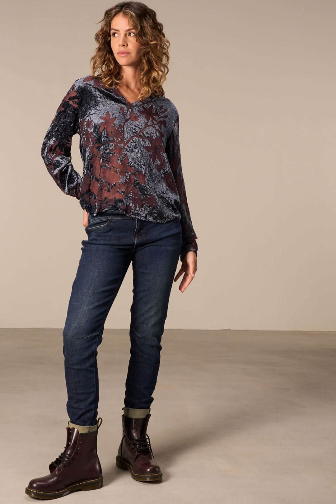 Femme portant un haut floral transparent avec un jeans cheville effilée et des bottes marron, style moderne.