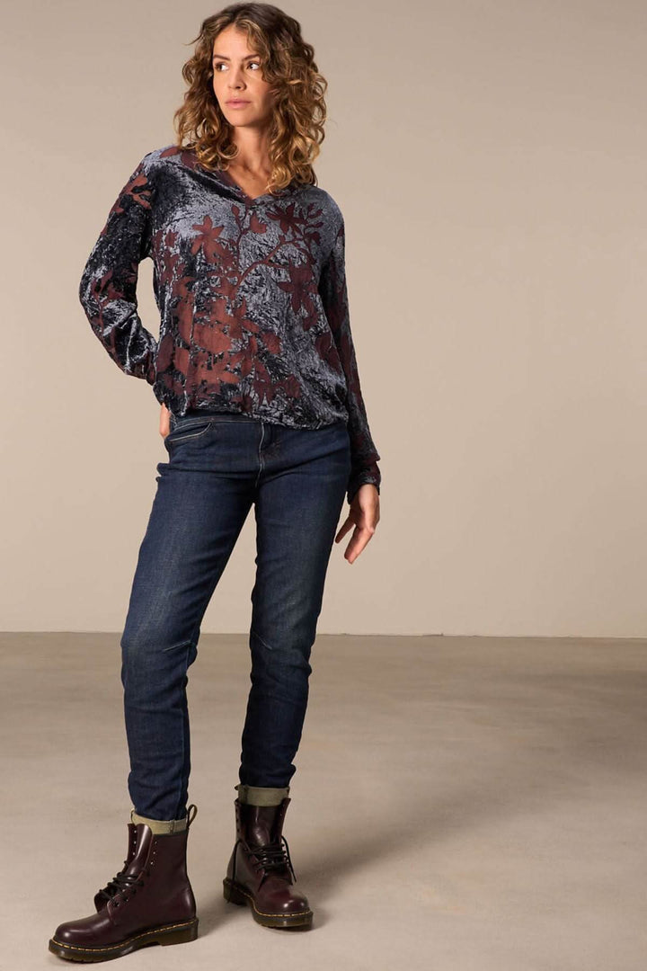 Femme portant un haut floral transparent avec un jeans cheville effilée et des bottes marron, style moderne.