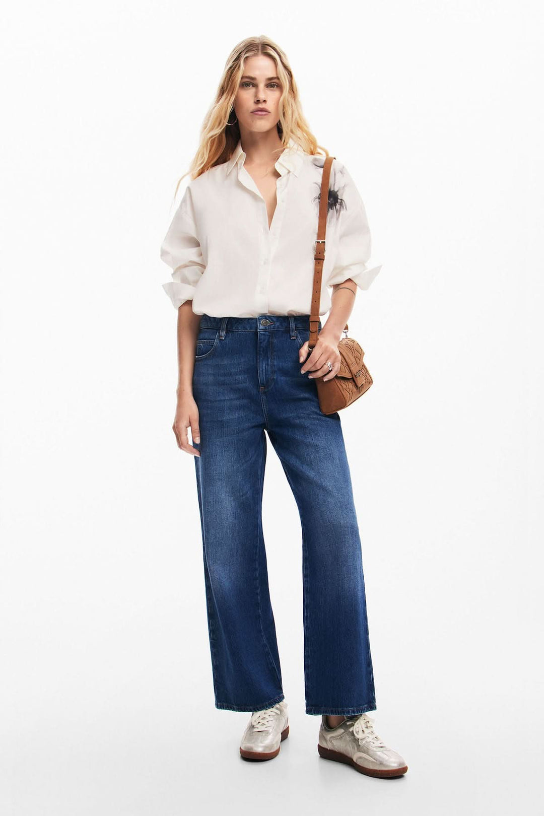 Femme portant un jean ample bleu avec une chemise blanche et des baskets, affichant un style décontracté.