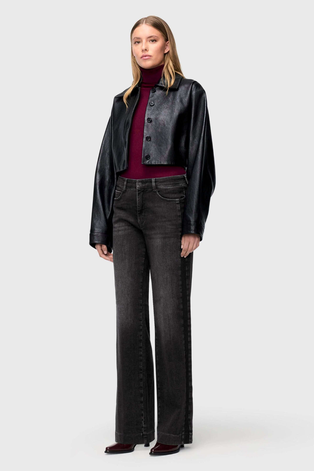 Modèle portant un jeans jambe large à effet délavé avec une veste en cuir noir et un pull bordeaux.