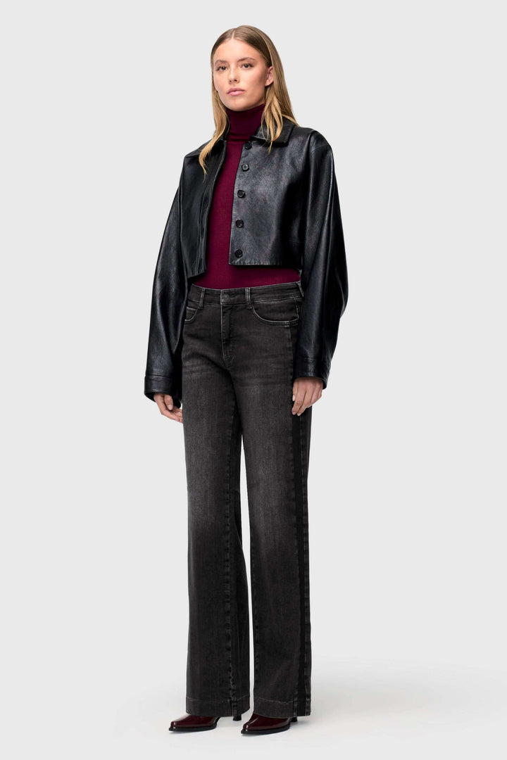 Modèle portant un jeans jambe large à effet délavé avec une veste en cuir noir et un pull bordeaux.
