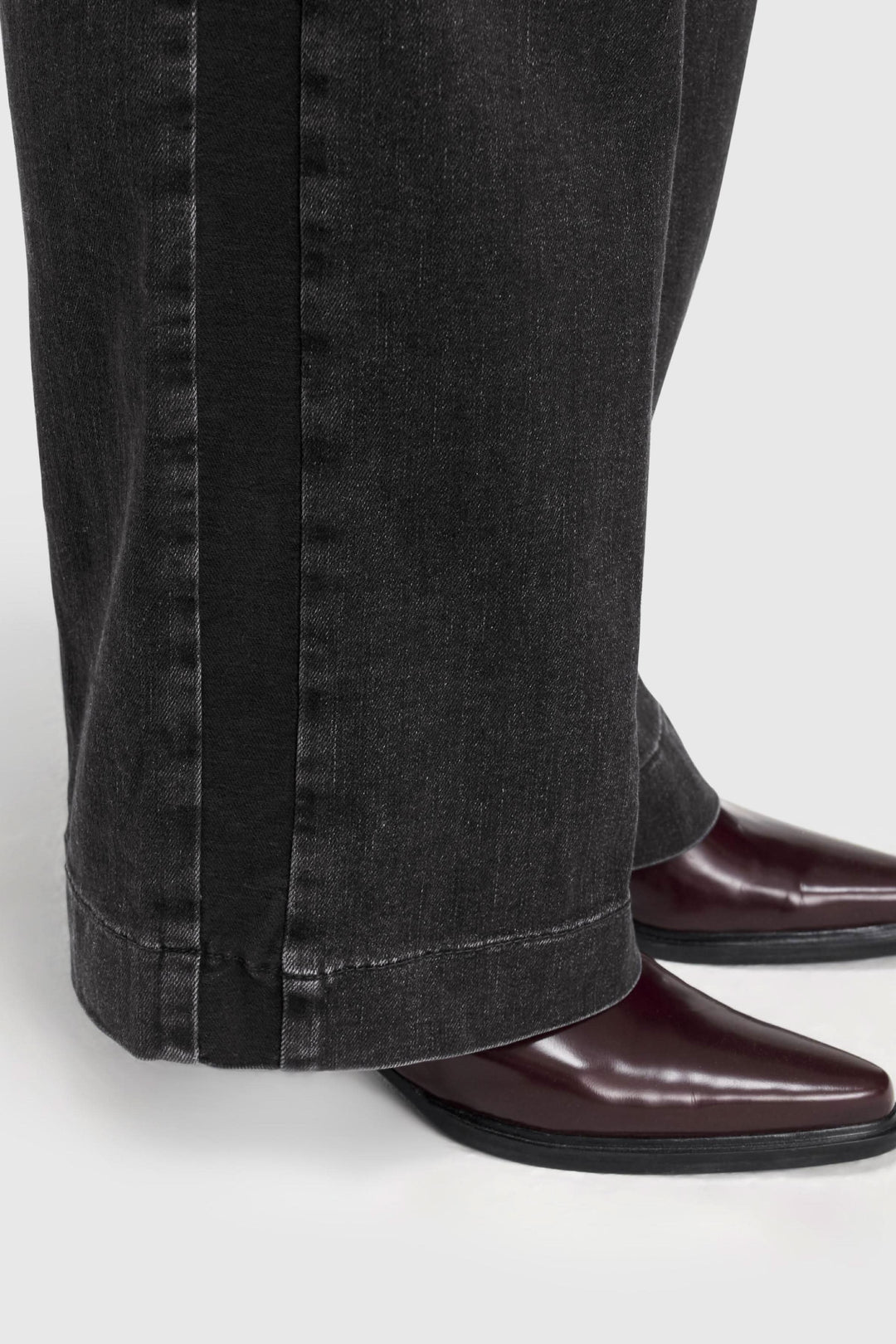 Jeans jambe large noir délavé avec coupe longue, porté avec des bottines pour un look rétro et décontracté.
