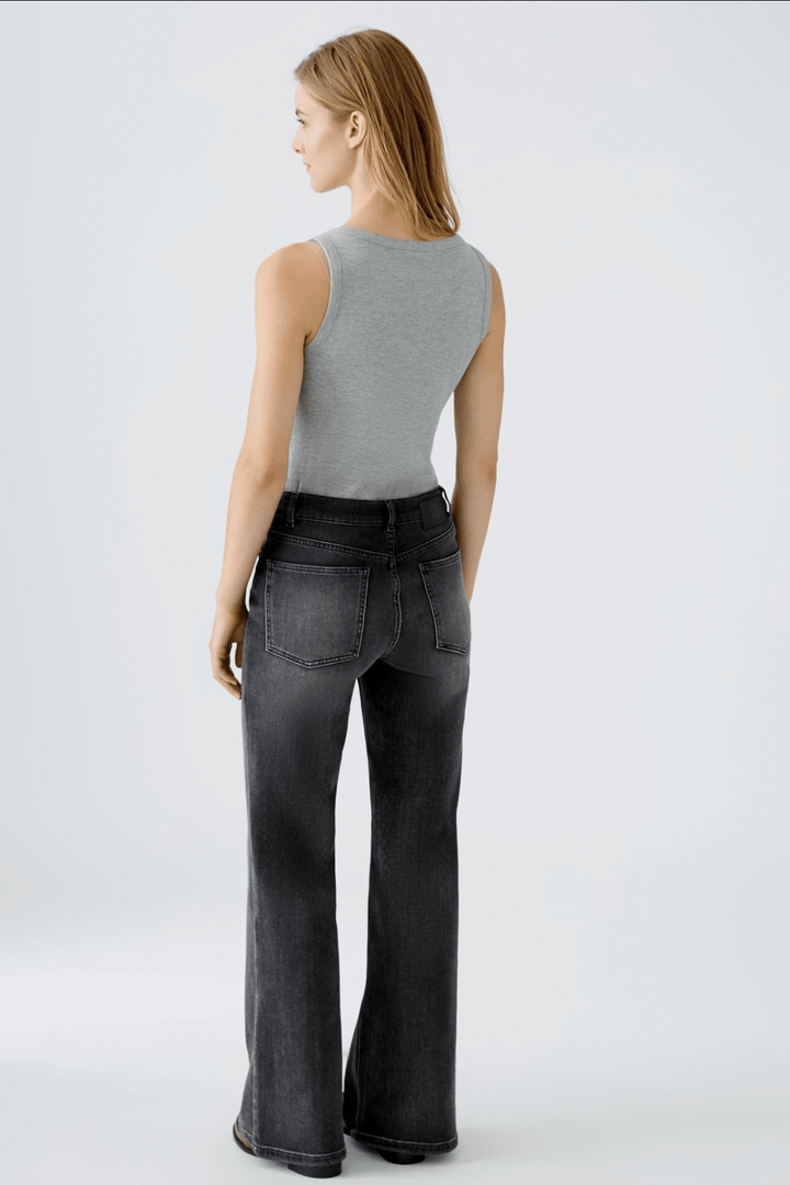 Femme vue de dos portant un tank top gris et des jeans évasés en denim noir, mettant en avant leur coupe moderne.