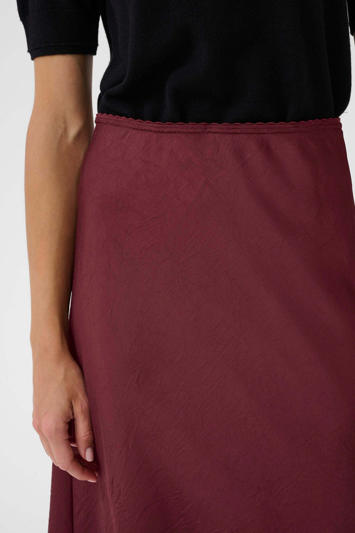 Détail d'une jupe midi fluide couleur bordeaux avec un tombé léger et une taille mi-haute, associée à un haut noir.