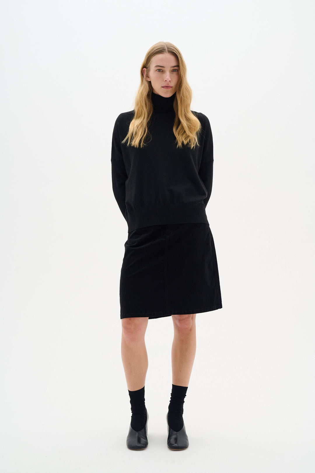 Modèle portant une jupe en velours noir et un pull noir, pour un look élégant et moderne.
