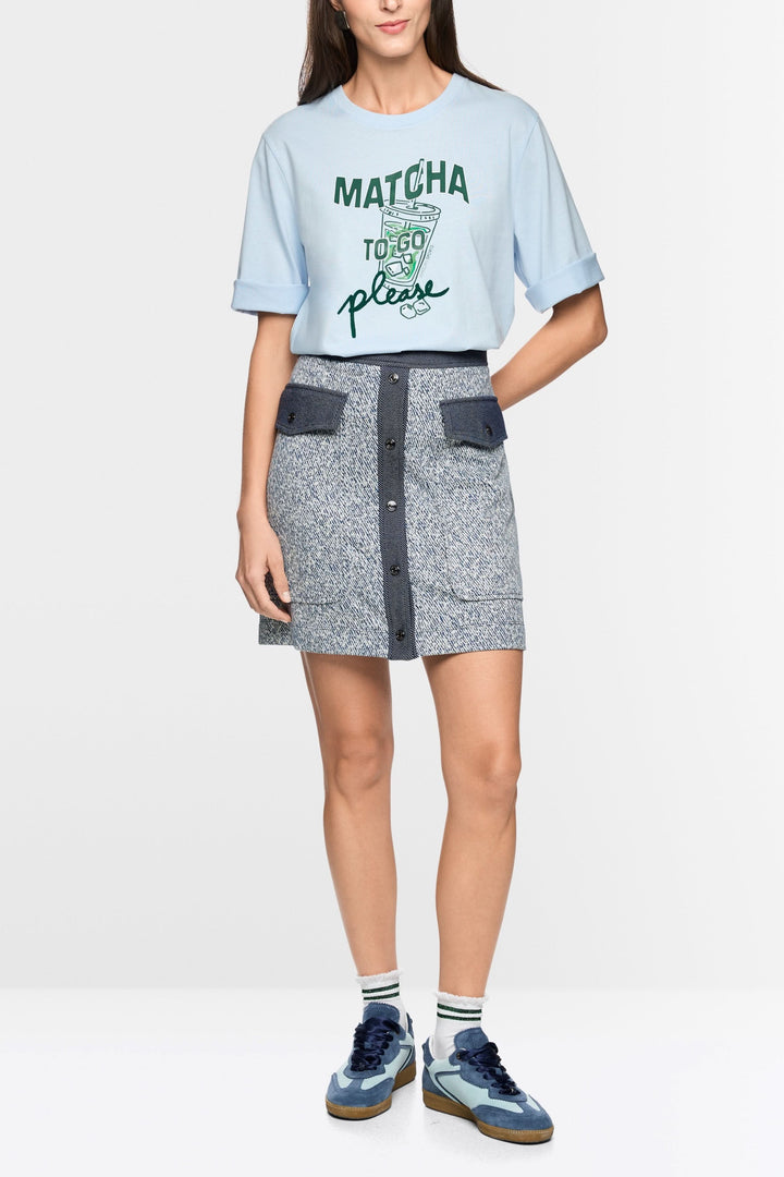 Jupe courte en viscose extensible avec fermeture boutonnée et poches à rabat, portée par un modèle décontracté.