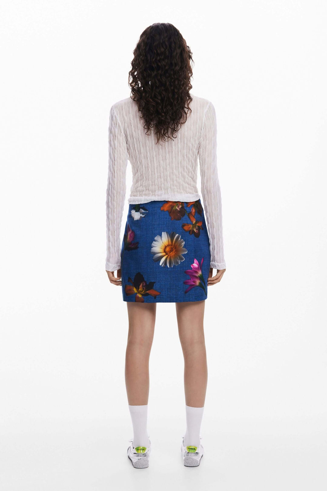Femme de dos portant une jupe courte à fleurs avec un haut à manches longues, style décontracté et moderne.