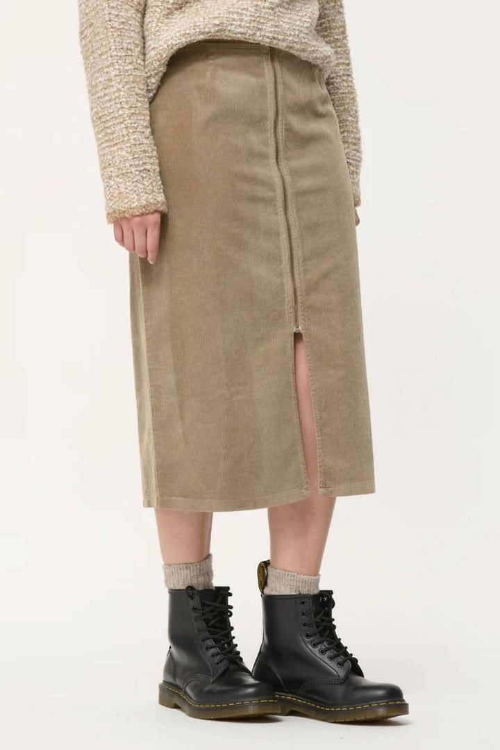 Jupe crayon en velours côtelé, taille haute, avec fente, portée avec des bottes noires.