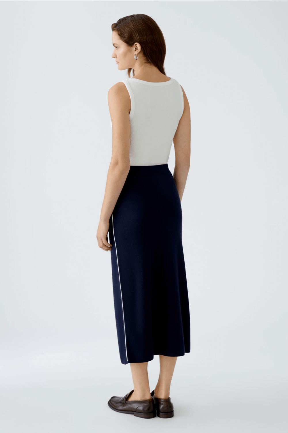 Femme portant une jupe droite en tricot, coupe midi, vue de dos, avec un haut sans manches blanc.