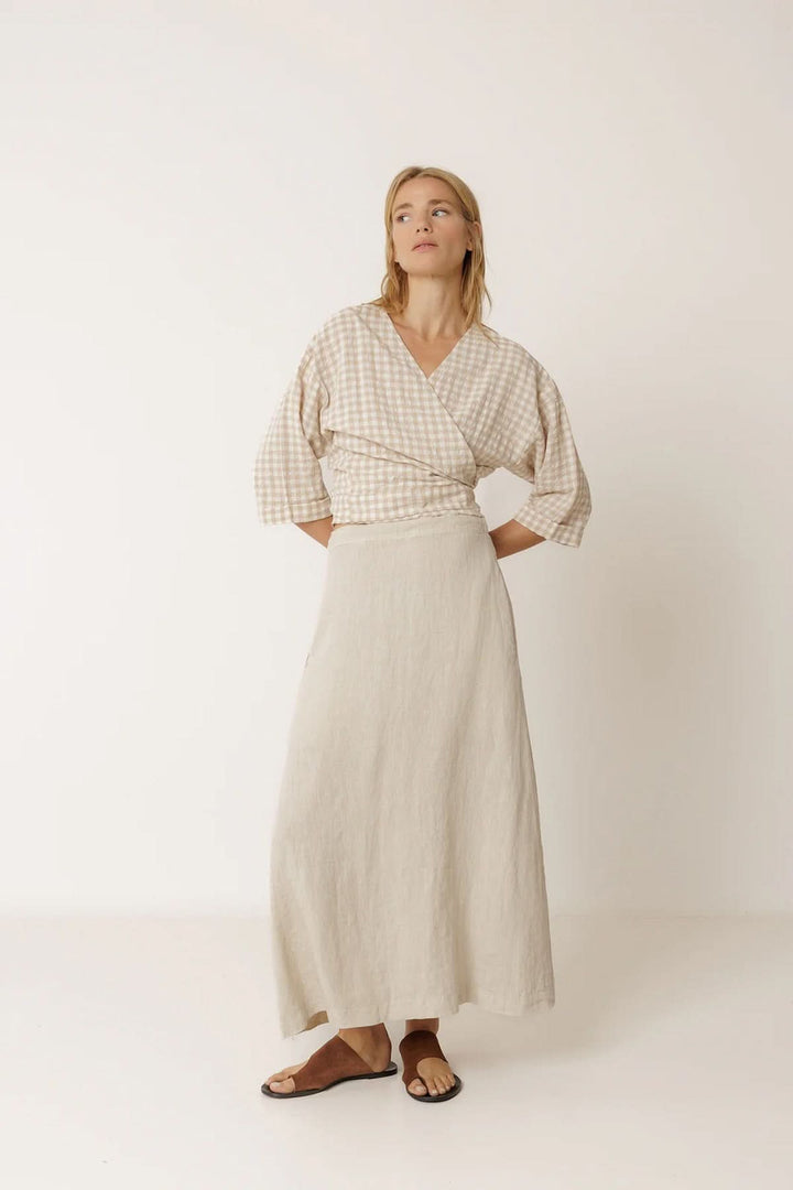 Femme portant une jupe midi fluide en lin beige élégante avec une coupe évasée, idéale pour un style naturel et intemporel.