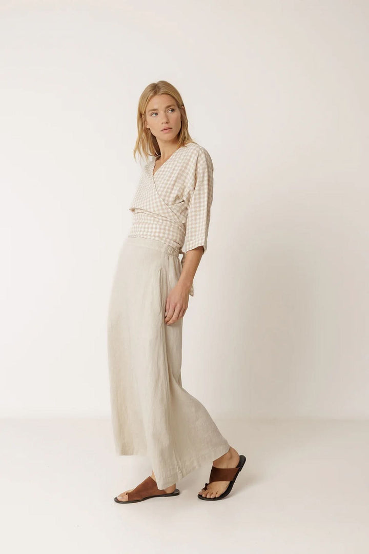Femme portant une jupe midi fluide en lin, élégante et légère, avec une chemise à carreaux, soulignant sa silhouette féminine et douce.