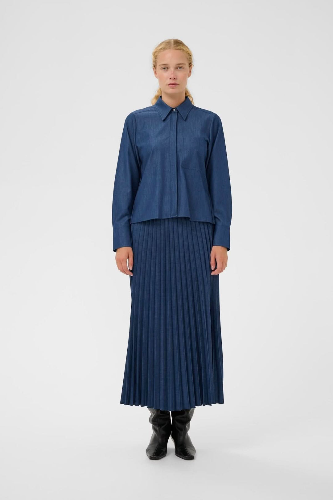Femme portant la Jupe midi plissée Cherrie, en tissu effet denim, coupe élégante mi-mollet, plis réguliers, style polyvalent.