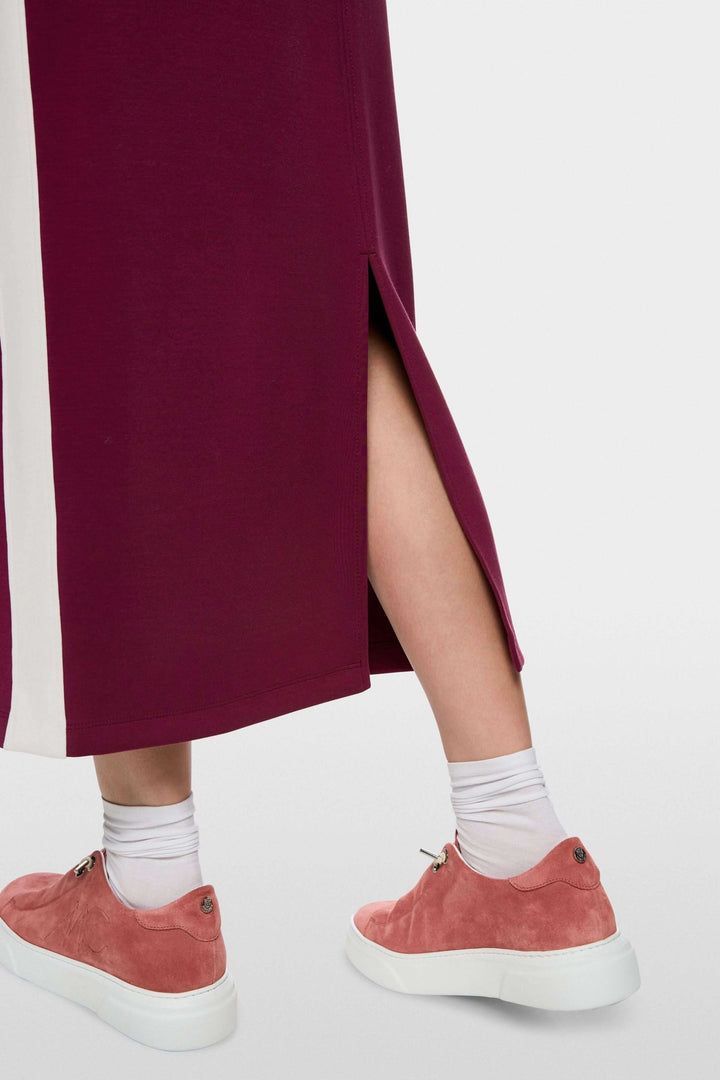 Jupe midi sportive avec fente arrière, bandes contrastées et chaussures roses visibles, idéale pour un look décontracté et stylé.