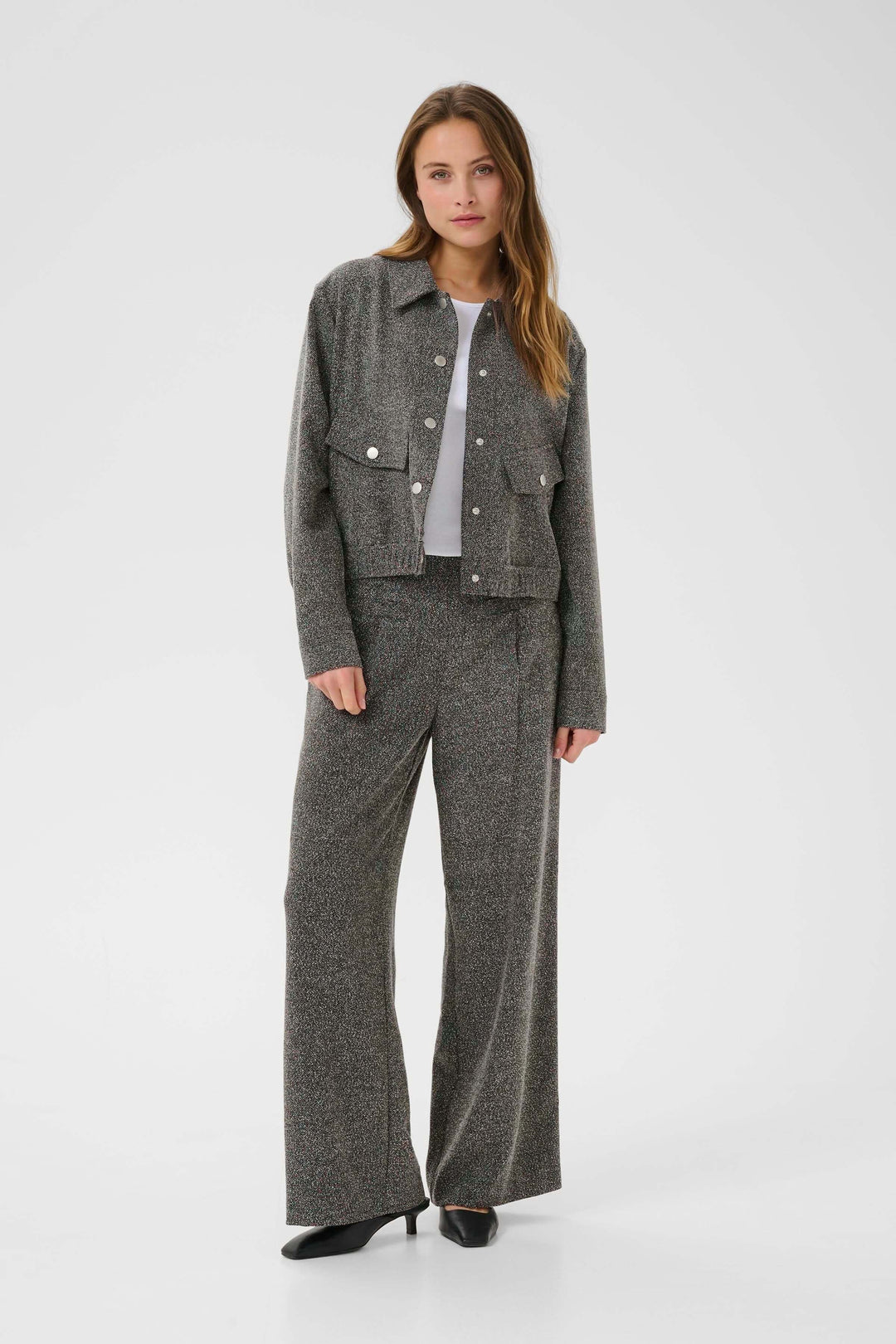 Femme portant un Manteau Alba court à poches à rabat et boutons contrastants, associé à un pantalon texturé.
