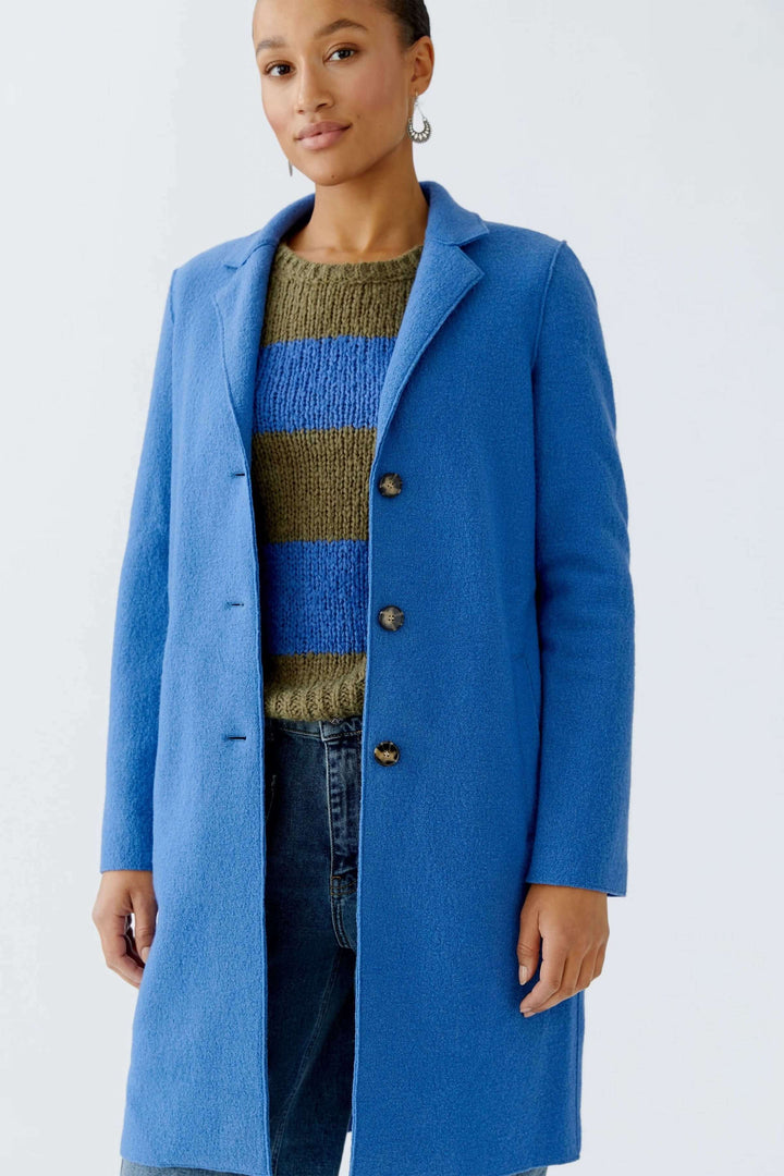 Femme portant le Manteau Mayson bleu, coupe droite et longue, sur un chandail rayé, look chic et décontracté.