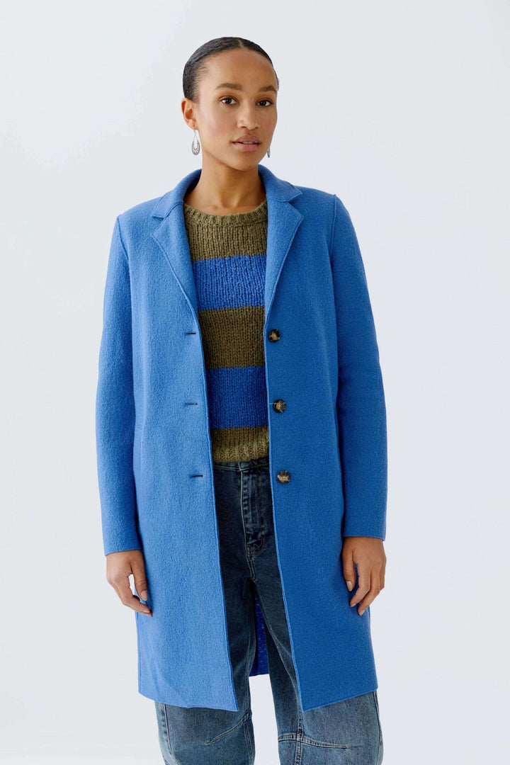 Manteau Mayson bleu, coupe droite et longue, col tailleur classique, porté sur chandail en maille rayé, look chic et décontracté.