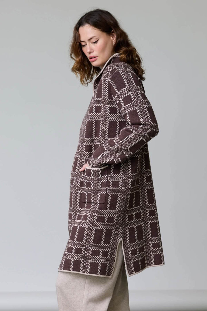 Femme portant un manteau en tricot à motif géométrique bicolore avec col à revers ouvert et poches plaquées, style moderne.