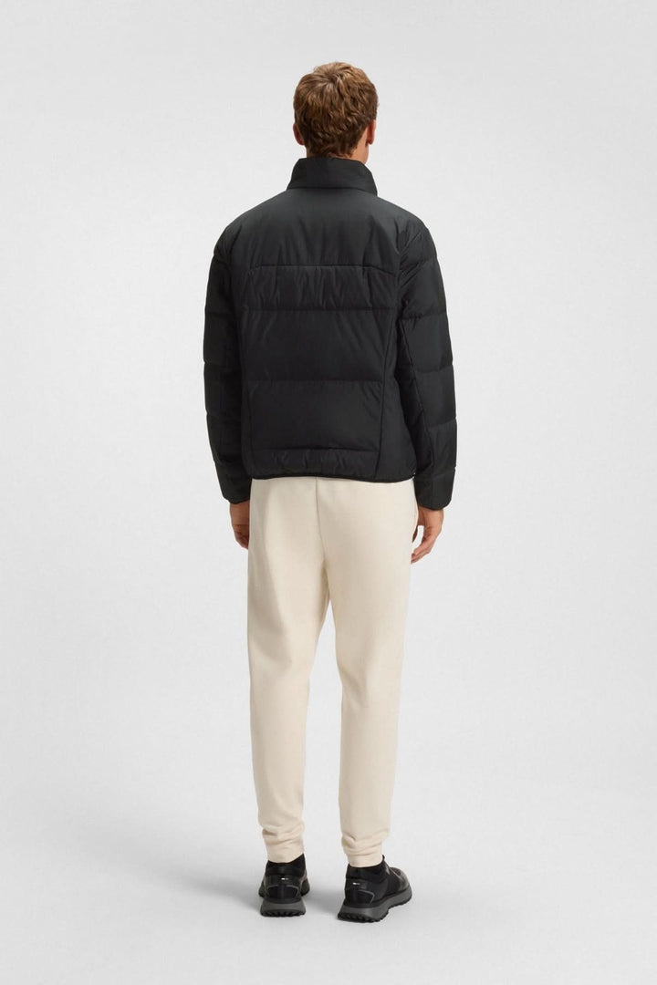 Homme portant un manteau matelassé déperlant en duvet avec poche sur la manche, vue de dos, design élégant et fonctionnel.