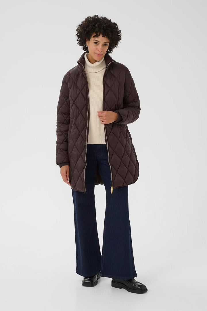 Femme portant un manteau matelassé à losanges avec fermeture zippée dorée, style chic et décontracté pour la mi-saison.