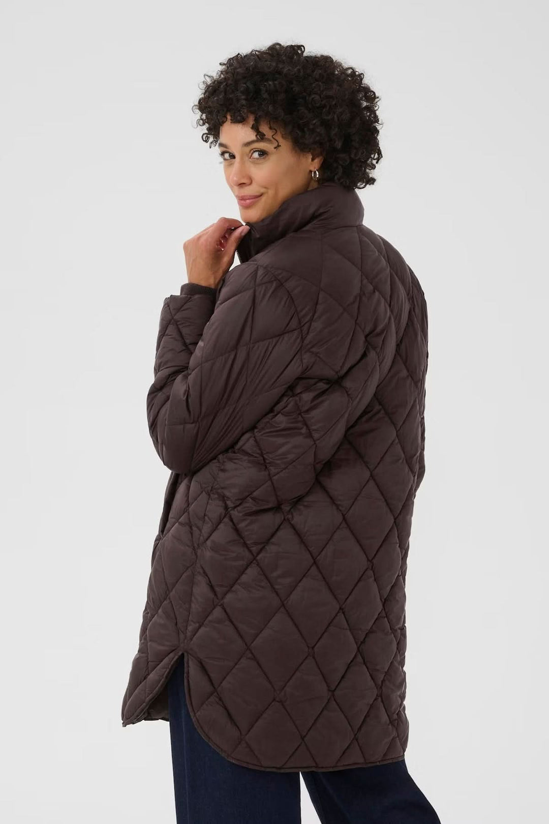 Femme portant un manteau matelassé à losanges, coupe longue, fermeture zippée dorée, idéal pour la mi-saison.