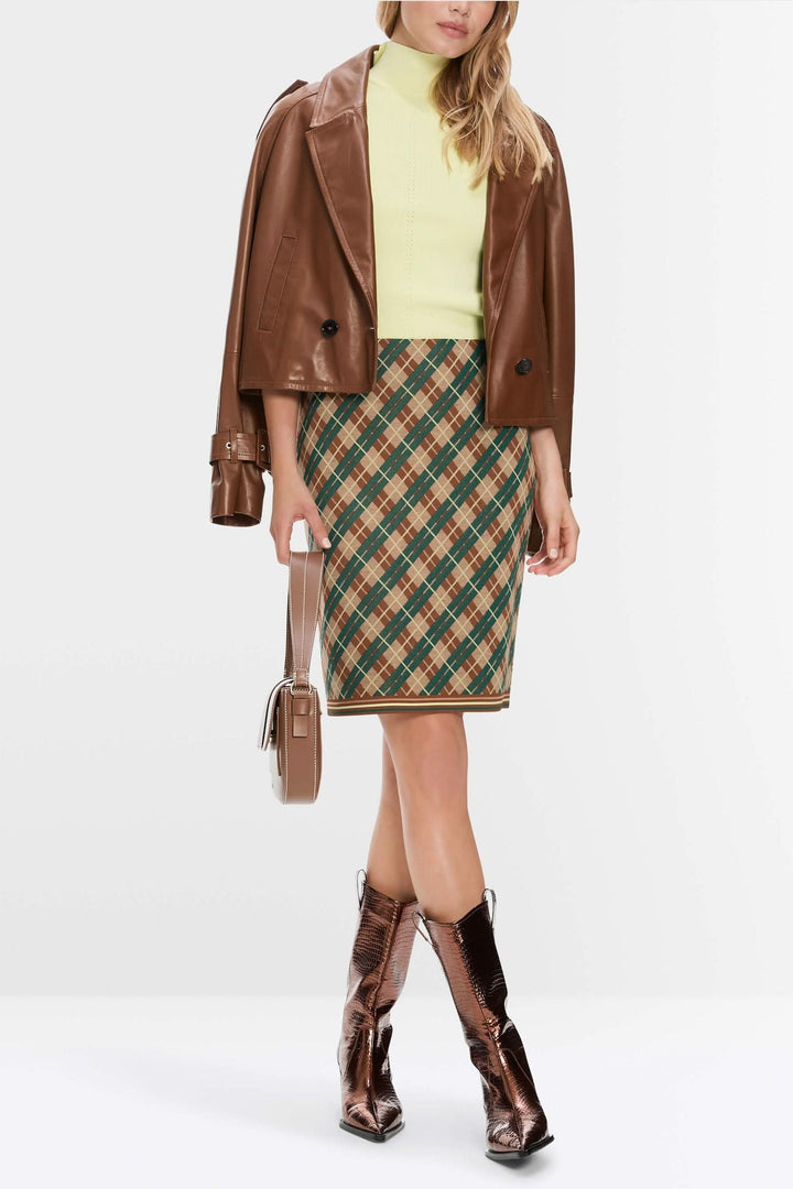 Femme portant une mini-jupe à carreaux argyle avec un pull vert et une veste en cuir marron.