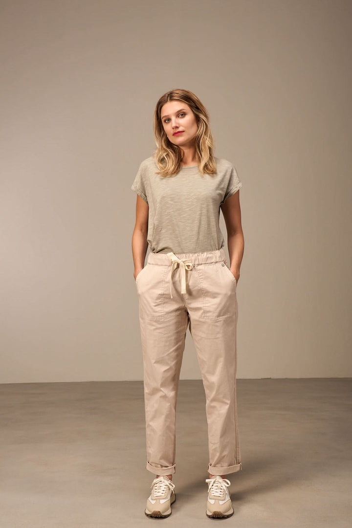 Femme portant un pantalon décontracté à taille élastique et un t-shirt gris dans un décor minimaliste.
