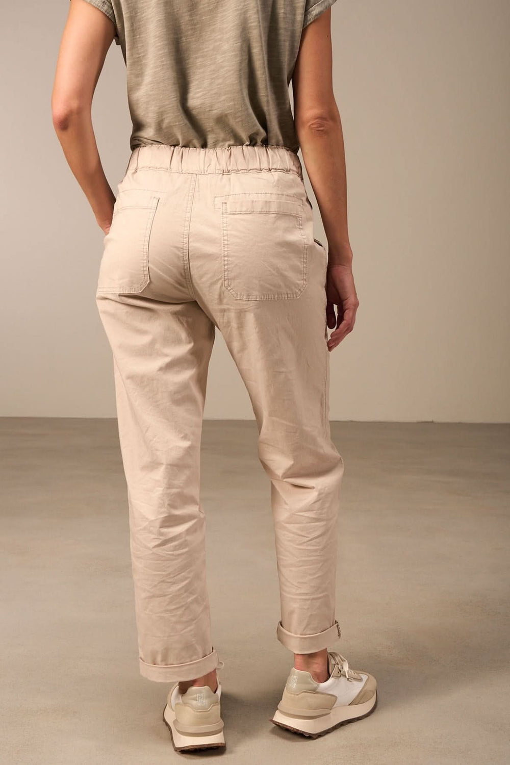 Femme portant un pantalon beige décontracté à taille élastique en vue arrière, style casual avec baskets.