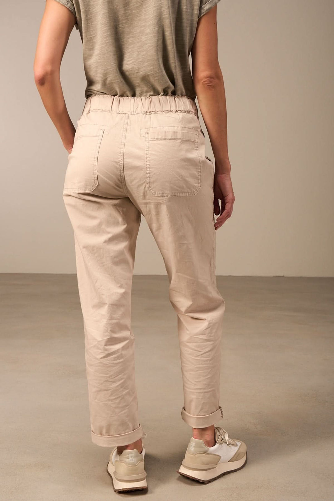 Femme portant un pantalon beige décontracté à taille élastique en vue arrière, style casual avec baskets.