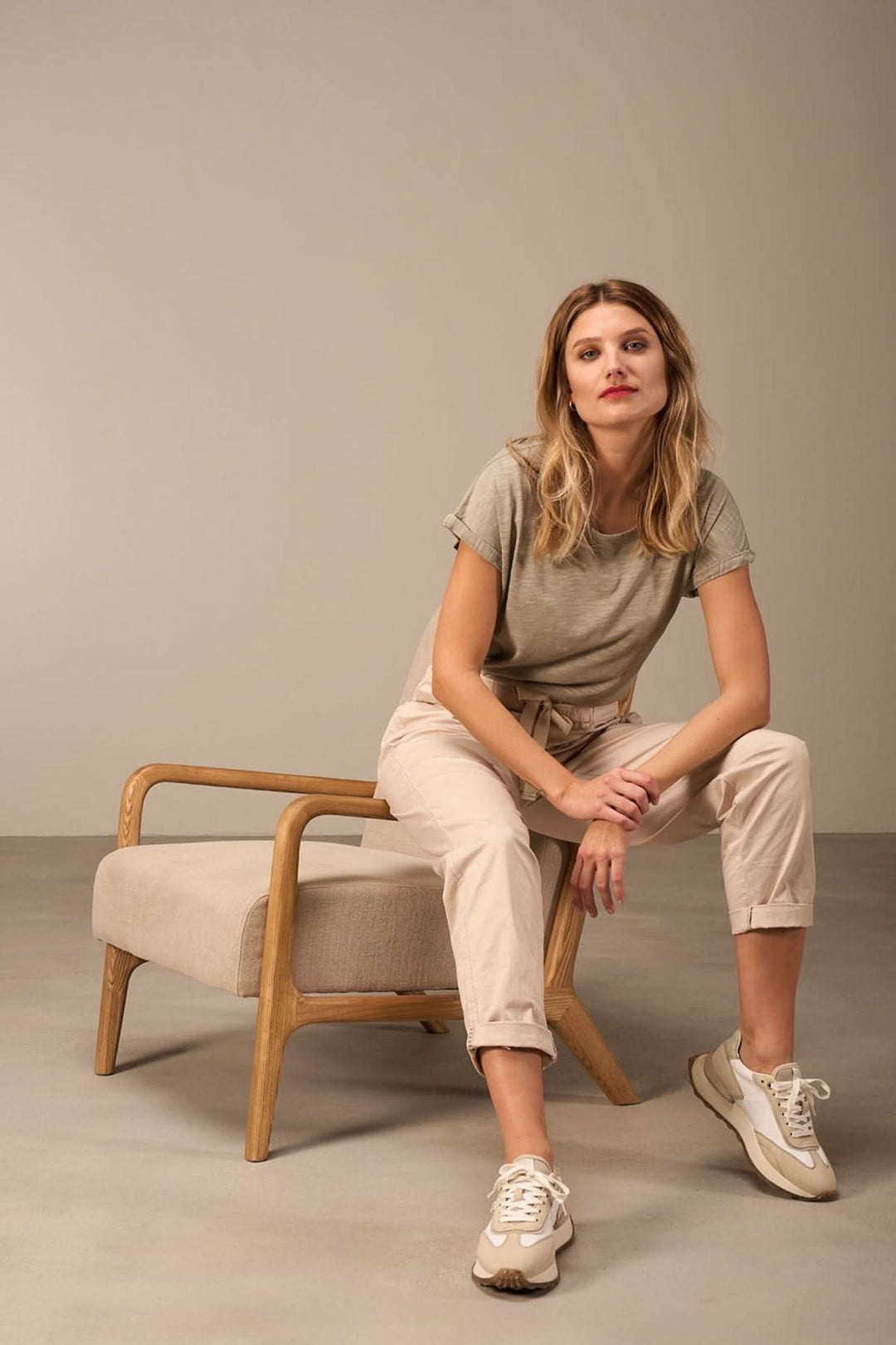 Femme assise sur une chaise, portant un pantalon décontracté à taille élastique et des baskets, dans un style moderne.