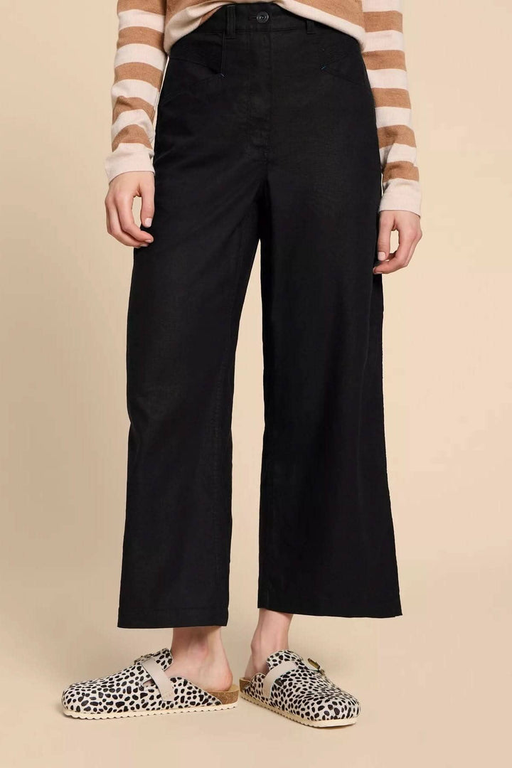 Pantalon Harper classique à jambe large en noir, porté avec un pull rayé et des mules imprimées.