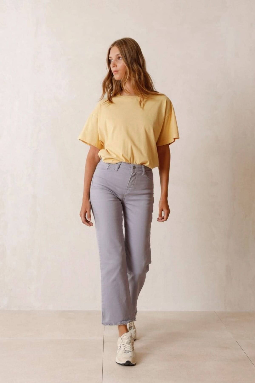 Femme en t-shirt jaune et pantalon gris décontracté marchant sur un fond neutre.