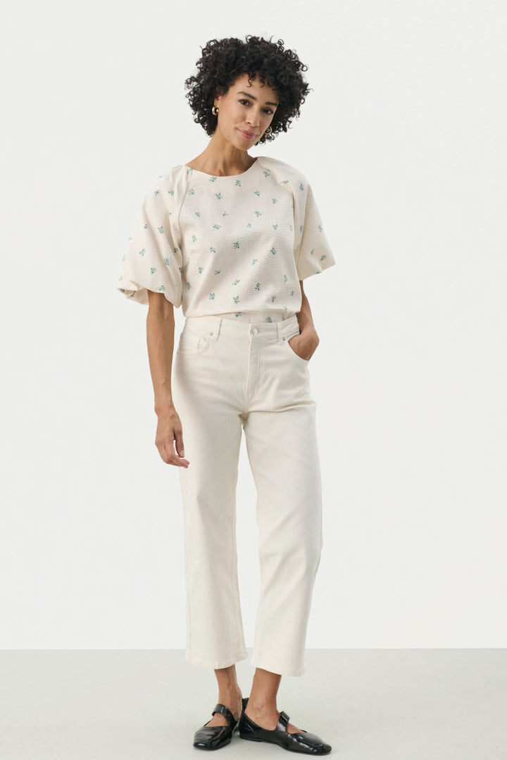 Femme avec t-shirt à motifs et pantalon évasé blanc, style décontracté et moderne, posture élégante.
