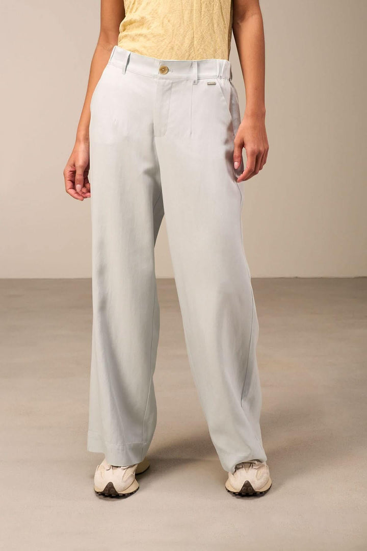 Pantalon large fluide bleu clair avec taille haute et plis marqués, porté avec un haut jaune et des baskets.