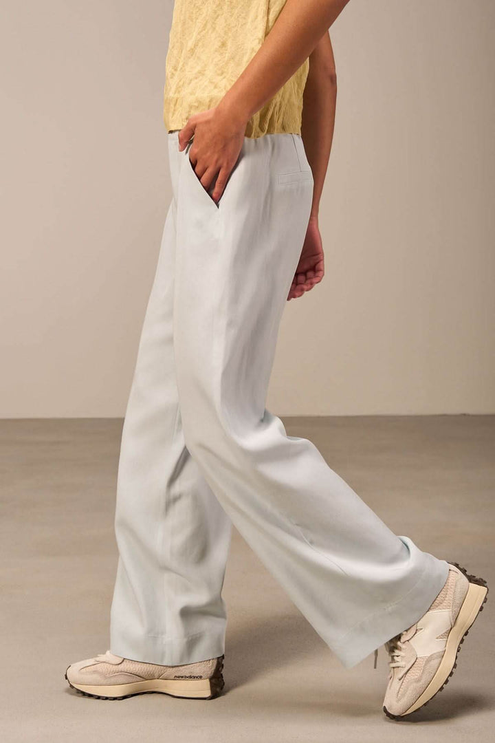 Pantalon ample bleu clair avec poches, taille haute, porté avec un haut noir et des chaussures décontractées.