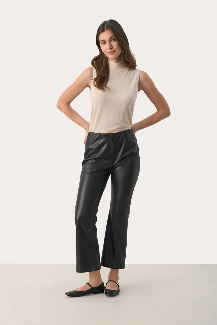 Pantalon noir en simili cuir, coupe évasée, taille haute, porté avec un haut beige, pour un look urbain et moderne.
