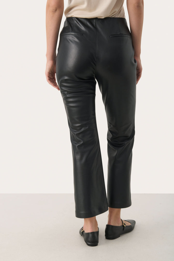 Pantalon Lorenza noir en simili cuir, coupe légèrement évasée, dos, porté avec des chaussures plates.