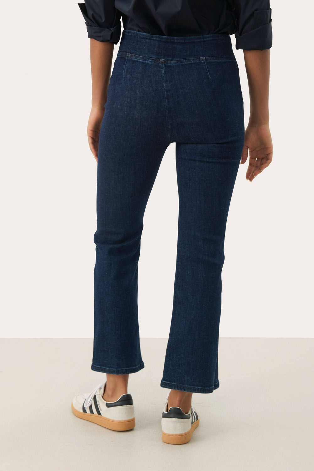 Vue arrière d'un Pantalon Nikela bleu avec coupe évasée et taille haute, porté avec des baskets blanches.