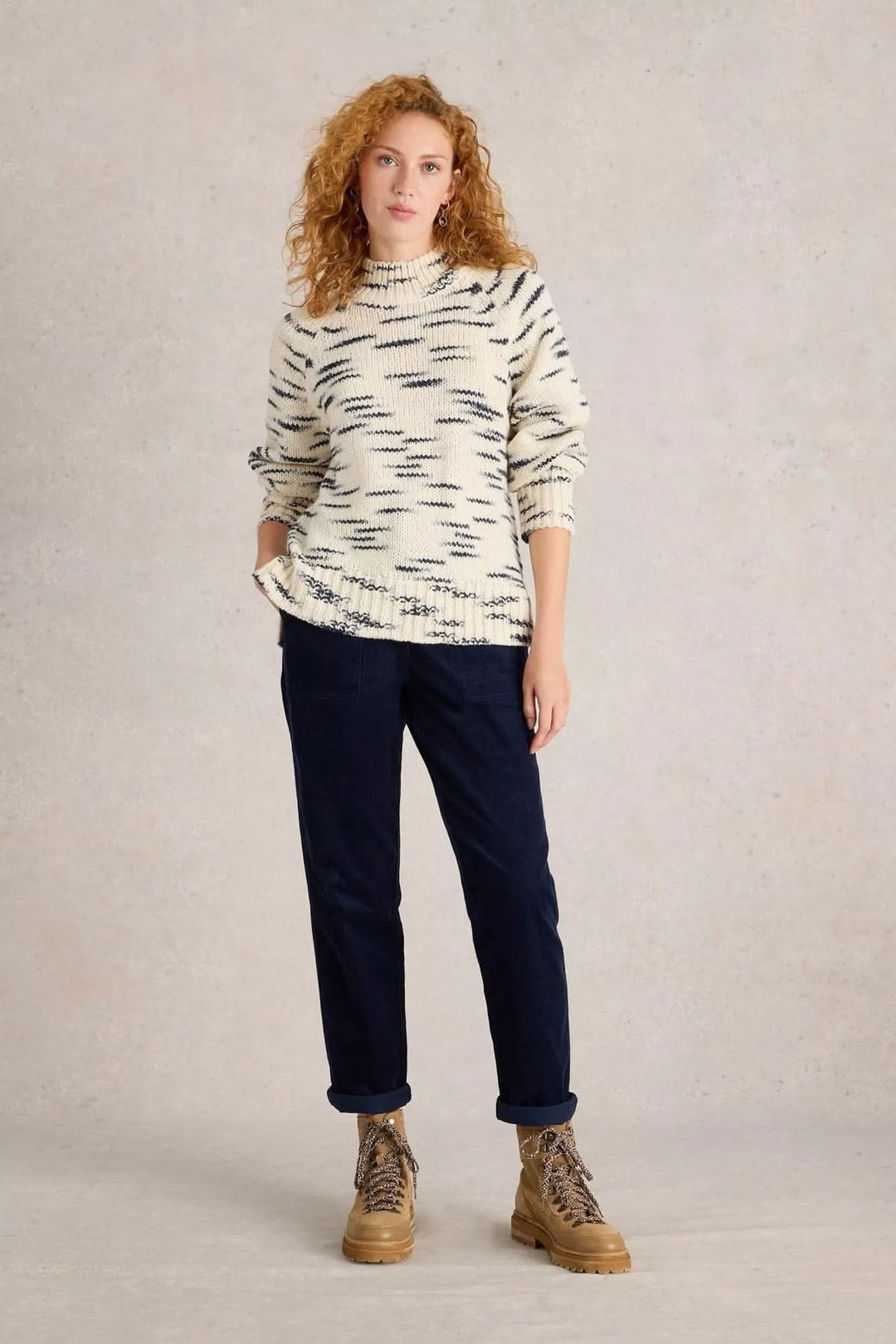 Femme portant le Pantalon Twister en velours côtelé bleu avec un chandail en maille et des bottes, look casual-chic automnal.