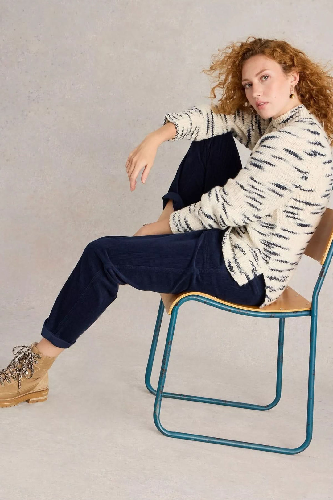 Femme portant un Pantalon Twister en velours côtelé avec chandail en maille, assise sur une chaise, look casual-chic de saison.