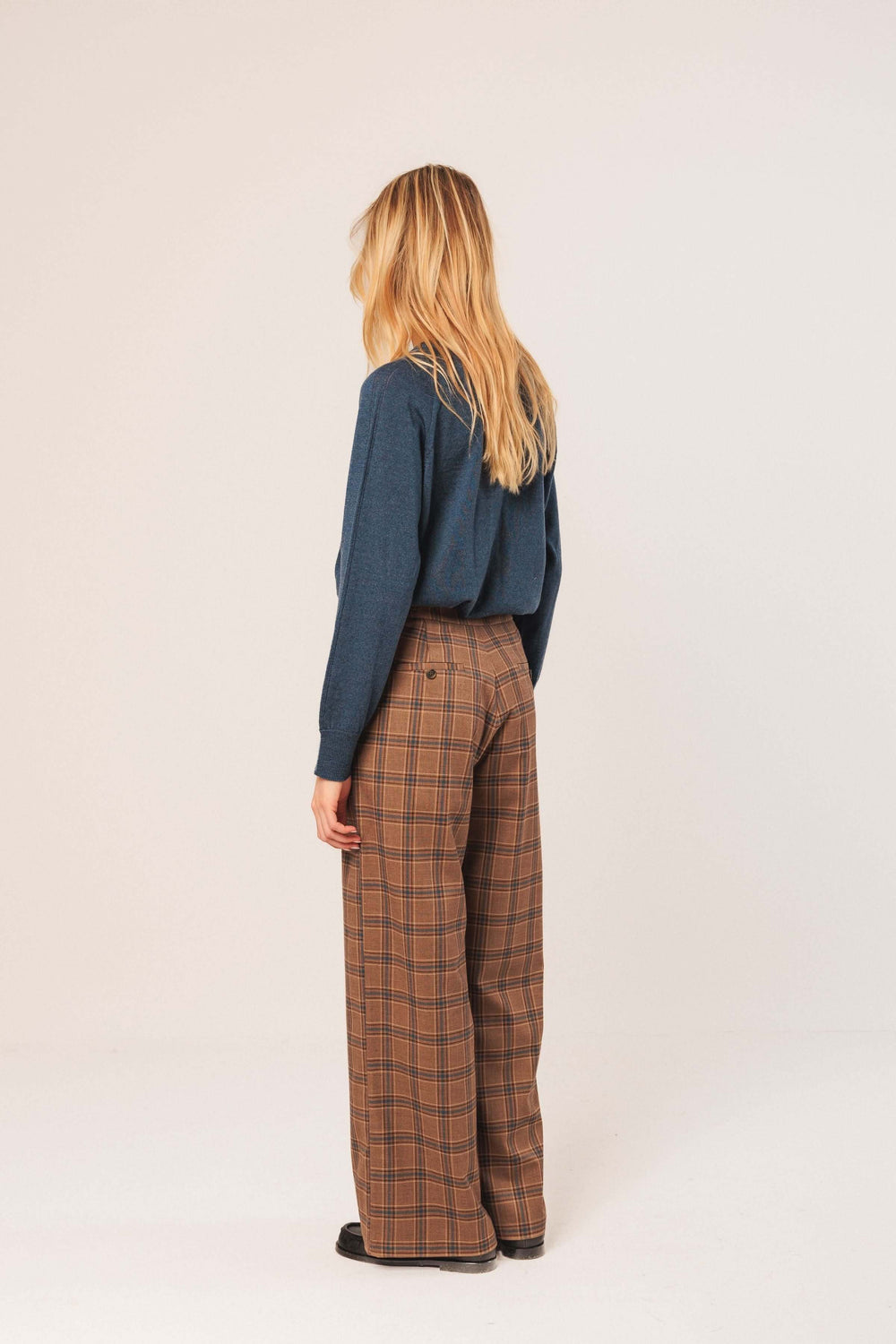 Pantalon à carreaux marron avec taille haute et coupe large, porté avec un chandail uni derrière.