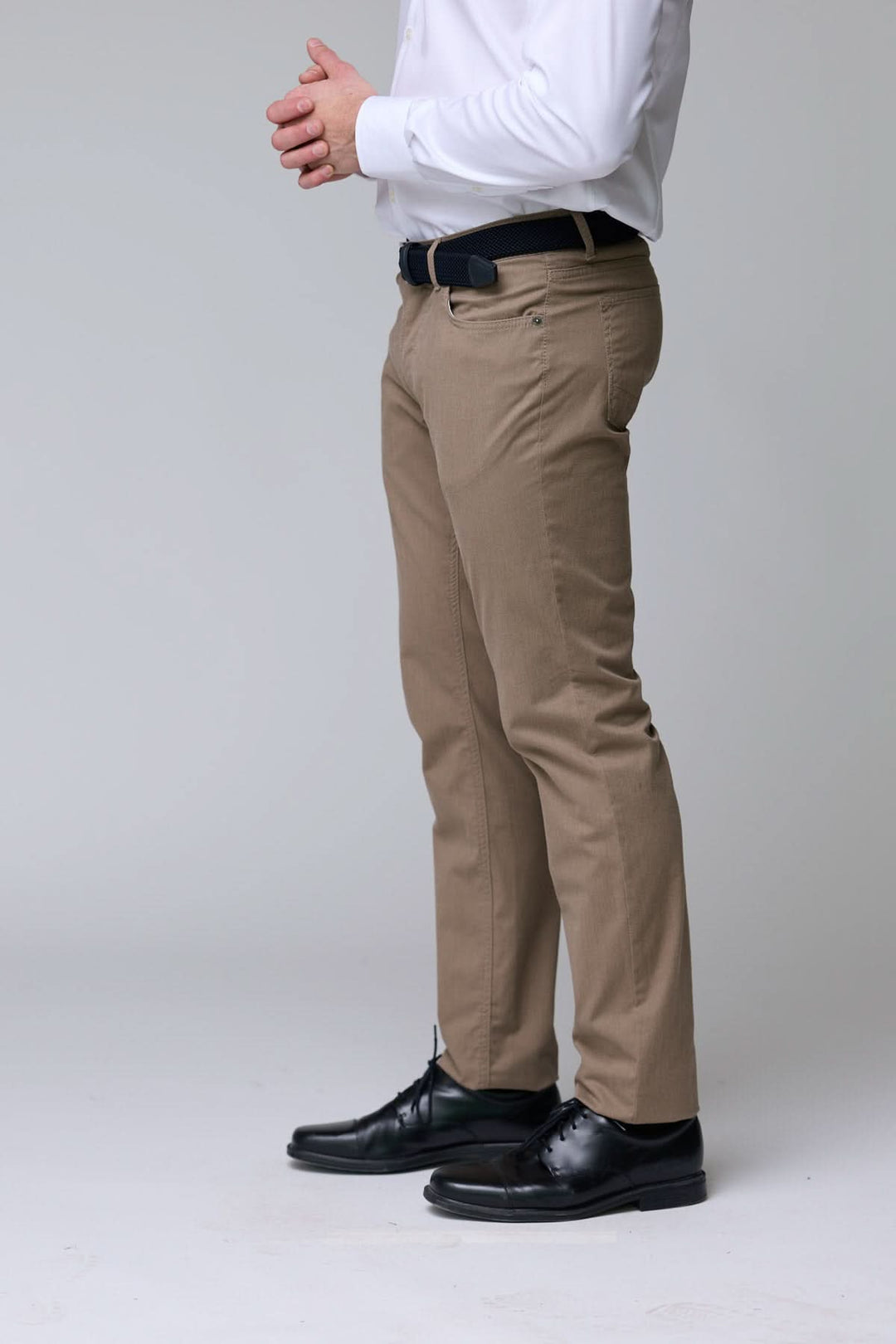 Homme portant un pantalon chino extensible beige, coupe ajustée, avec une chemise blanche et des chaussures noires élégantes.
