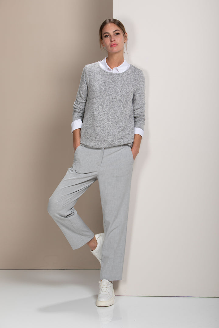 Femme portant un pantalon coupe droite gris, style élégante pour le bureau, avec chandail gris et chemise blanche.