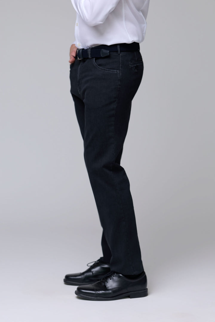 Homme portant un pantalon denim extensible noir, coupe ajustée, associé à une chemise blanche, style moderne et élégant.