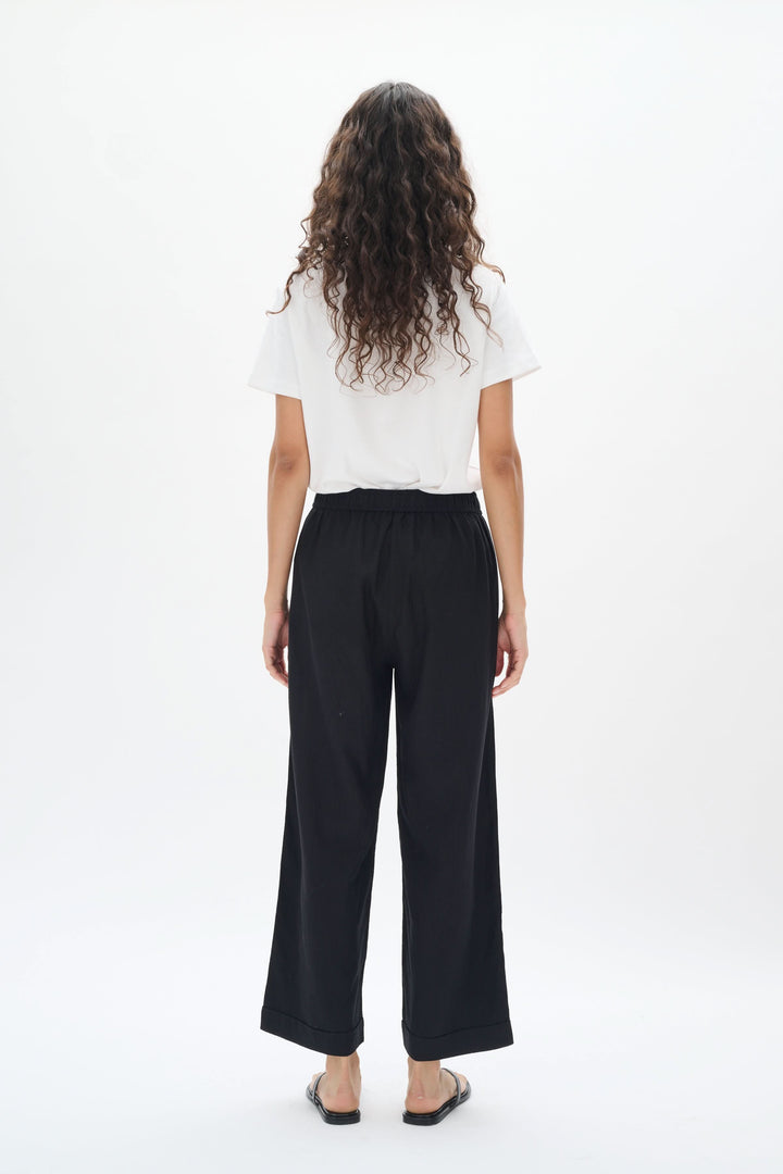 Femme vue de dos portant un pantalon en lin noir à taille élastique et jambes larges.