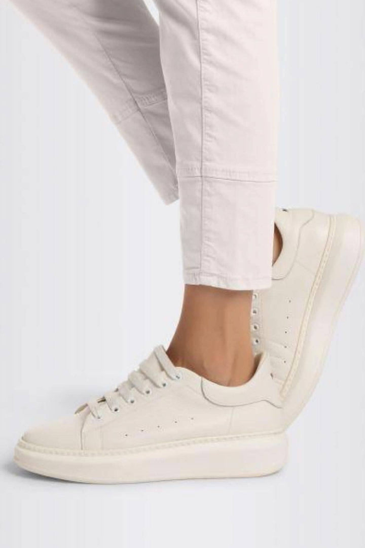 Sneakers blanches élégantes portées avec un pantalon fuselé rose, offrant un look chic et décontracté.