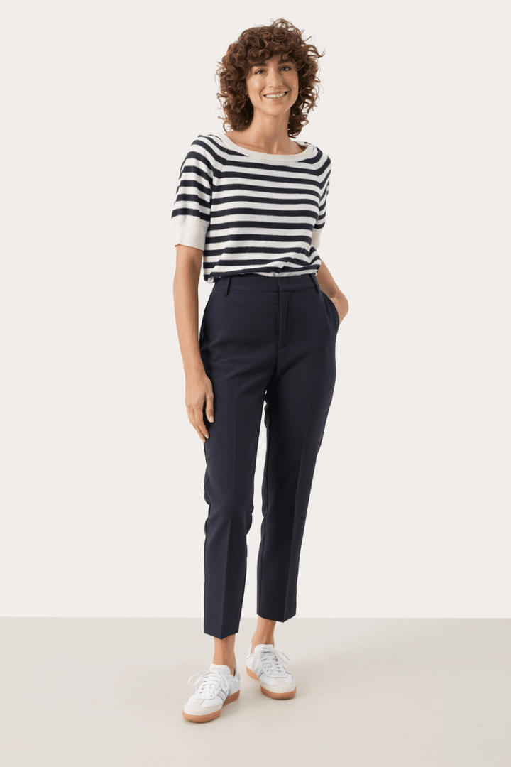 Femme souriante portant un pantalon habillé Urbana avec un t-shirt rayé, créant un look chic et décontracté.