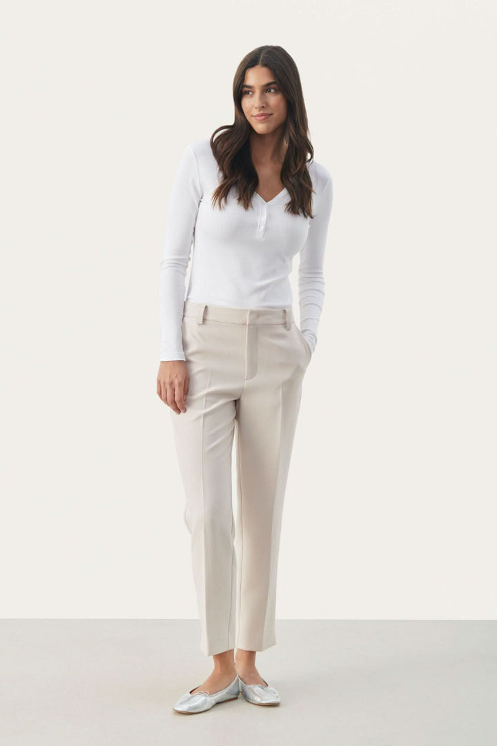 Femme portant un pantalon habillé Urbana beige avec une coupe fuseau élégante et un top blanc, look sophistiqué.