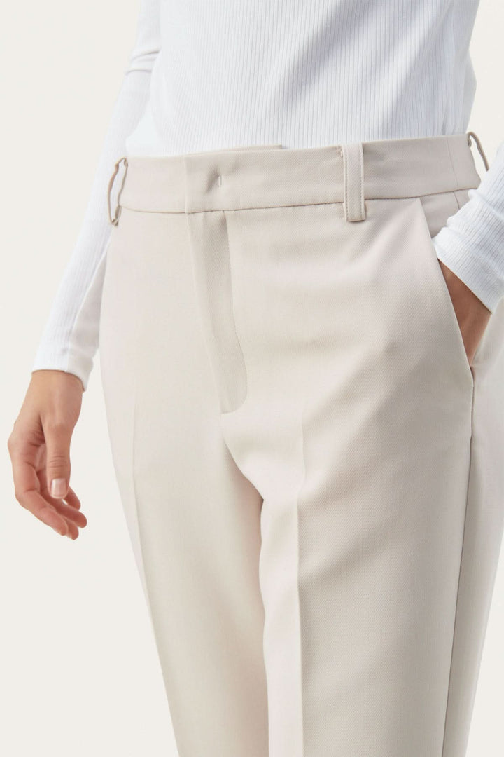 Détail du pantalon habillé Urbana avec coupe fuseau élégante et poches en biais, en tissu léger et fluide.